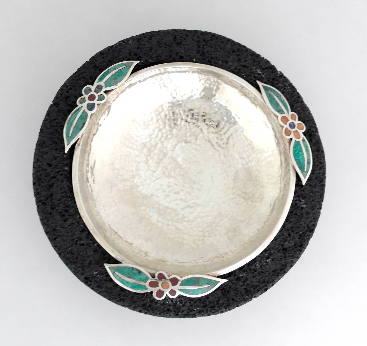 Being offered is a circa 1990 serving bowl by Emilia Castillo of Taxco, Mexico. Hammered bowl with three floral motifs, placed in a lava rock formed bowl. Silver bowl is removable for cleaning. Dimensions: 10 inches diameter. Marked as illustrated.