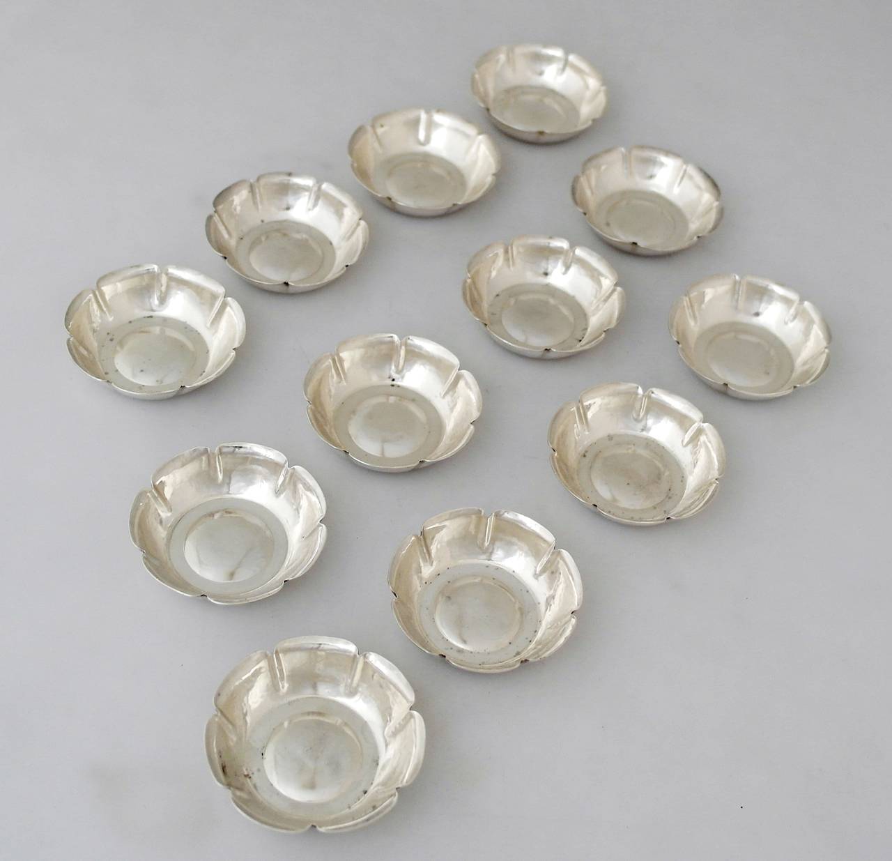 Being offered are a set of 12 circa 1920 nut or mint or wasabi dishes by Joel Hewes of Titusville, Pennsylvania. Entirely hand-wrought, lobed dishes made by a prominent and collecteded silversmith during the Arts & Crafts movement. Dimensions:  2