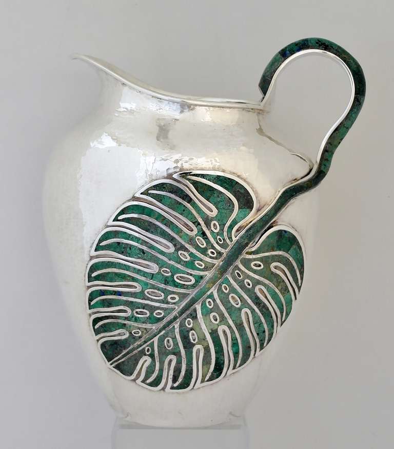 Being offered is a circa 1990 sterling silver and malachite pitcher by Emilia Castillo of Mexico, entirely hand hammered with a highly stylized and exotic applied malachite leaf and with applied malachite hammer.  Height a tall 11 inches.  Weight a