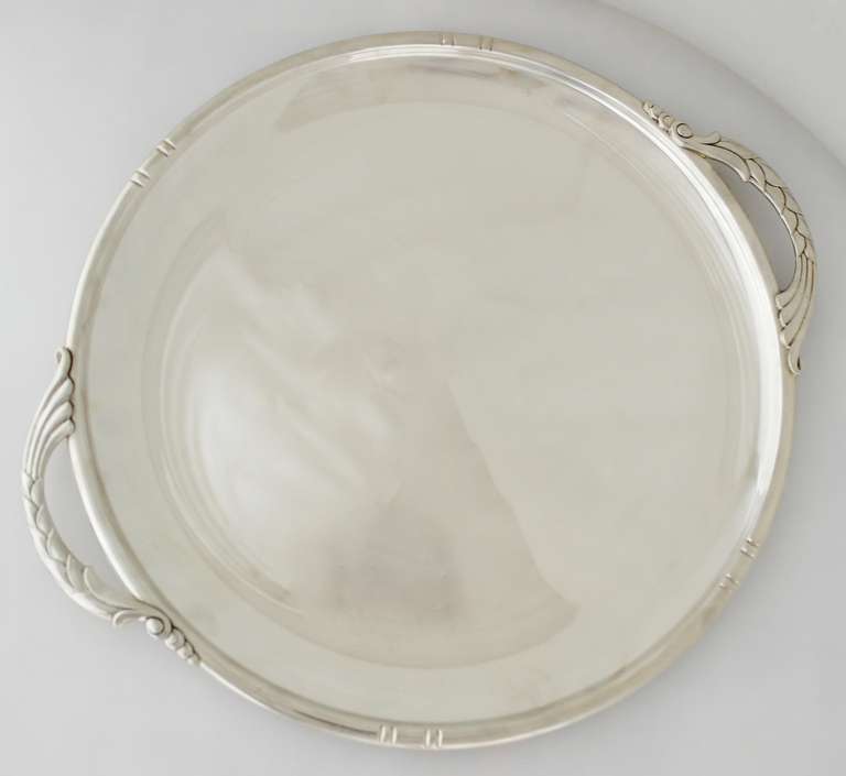 Being offered is a circa 1930s sterling silver tray by Randahl Shops of Chicago, Illinois. Of Danish influence, the round tray boasts a modernist look, with symmetrical incised vertical lines at the rim; embossed leaf and scroll handles. Dimensions: