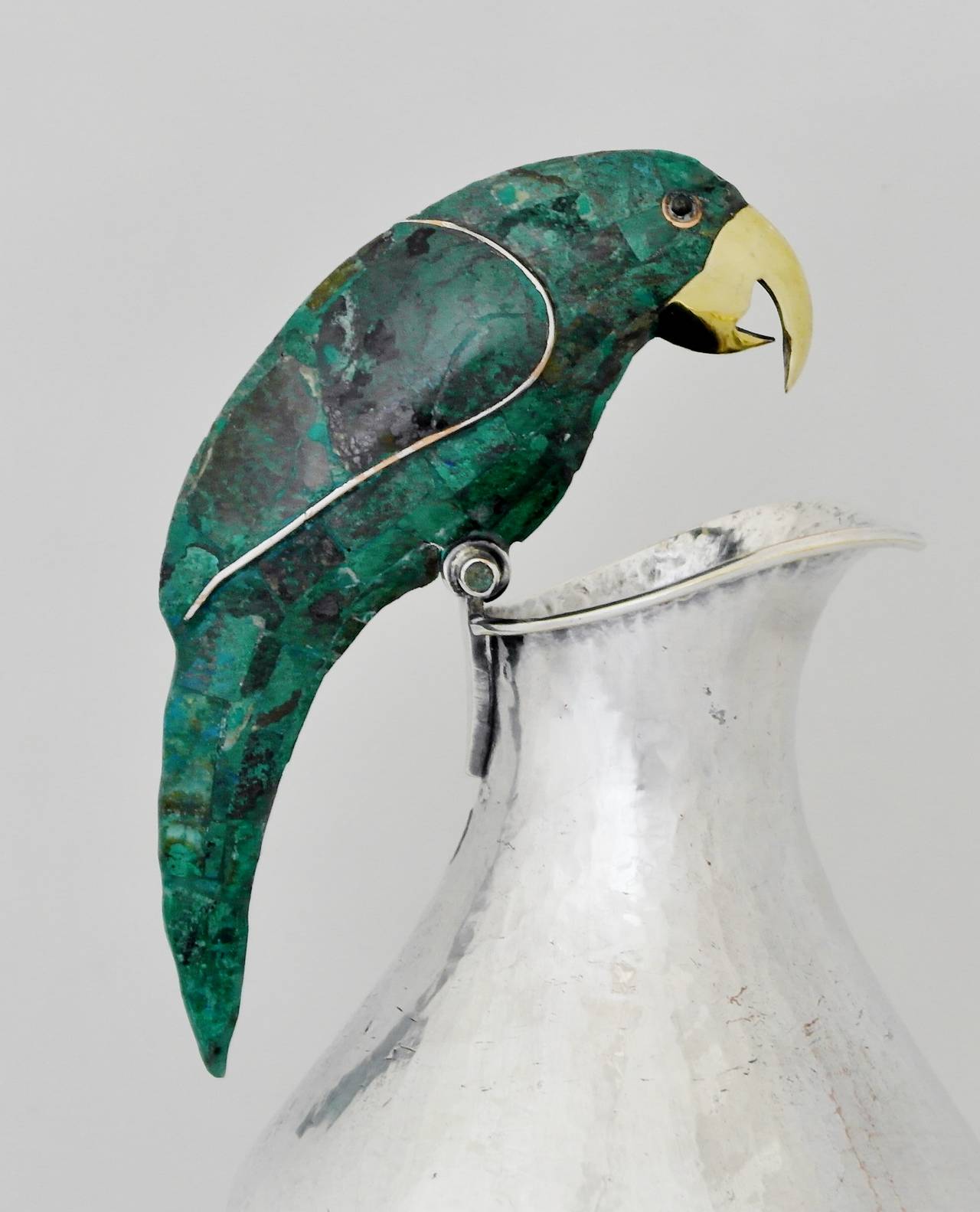 Being offered is a circa 1970 silverplate pitcher by Los Castillo of Taxco, Mexico. Entirely hammered heavy gauge object with parrot handle decorated by azur malachite inlay; brass beak. Dimensions: 8 inches tall x 5 inches diameter. Marked as