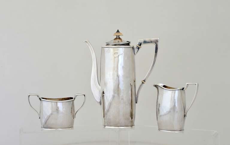 Being offered is an exceedingly rare circa 1930 sterling silver coffee/tea set by James T. Woolley of Boston, Massachusetts; colonial inspired; hand wrought in the arts & crafts method; rectangular shaped service with ivory insulators &