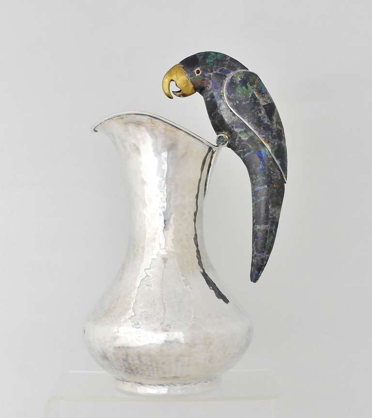 Being offered is a contemporary silverplate pitcher by Los Castillo of Taxco, Mexico. Entirely handmade heavy piece with hammered texture & a parrot handle with multi-stone inlay. Dimensions: 11