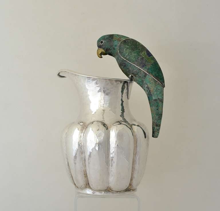 Being offered is a circa 1980 silverplate pitcher by Los Castillo of Taxco, Mexico, ribbed form with hammered texture & malachite stone inlay on the figural parrot handle. Dimensions: 10 1/2