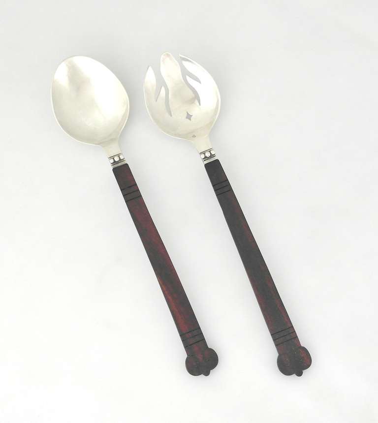 Being offered is a pair of circa 1960s salad servers by Los Castillo of Taxco, Mexico. Carved rosewood handles in the Aztec design attached to hand wrought sterling silver bowl & tines with three applied beads on the neck. Dimensions: 12
