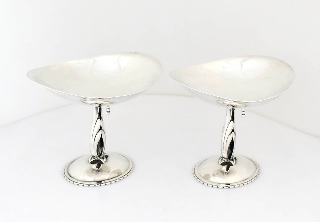 Being offered is a rare and early pair of circa 1920 sterling silver tazzas by Cellini Craft of Chicago, Illinois. Hand-wrought tazzas decorated with double leaf stems and hand worked spray of seeds; light hammered oval trays. Dimensions: 6