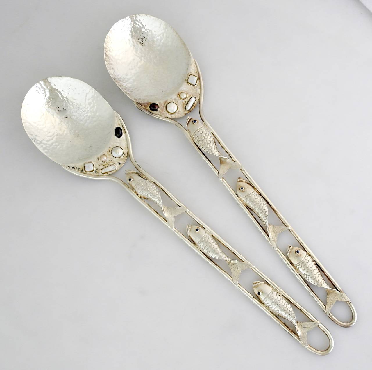Being offered are a pair of circa silver plate serving spoons by Emilia Castillo of Taxco, Mexico. Large hand-wrought servers; pierced handles with fish motifs; applied white and black pearls on the hammered bowls. Dimensions: 16 3/4