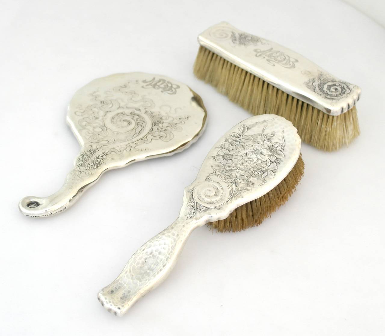 Being offered are a circa 1888 sterling silver 3 piece grooming dresser set by Whiting of New York. Comprising a hand mirror & two brushes (clothing and hair), all with acid-etched floral, scroll & spiral motifs; one brush has delicate hammered