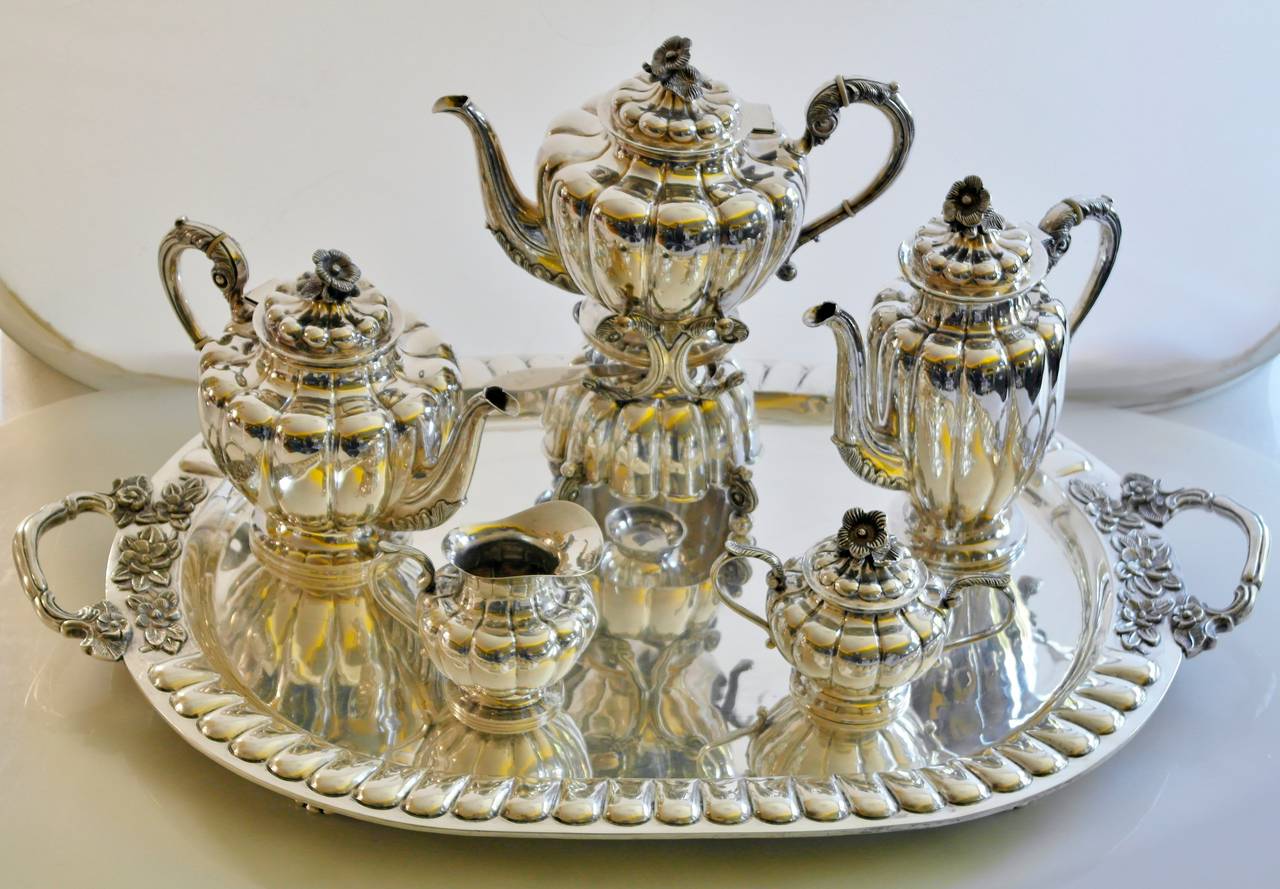 Being offered is a circa 1950 sterling silver tea and coffee set by Sanborns of Mexico City, comprising teapot, coffee pot, kettle on lamp Stand, creamer, sugar bowl, waste bowl and two-handled tray, all with attenuated lobed bodies and leaf-capped