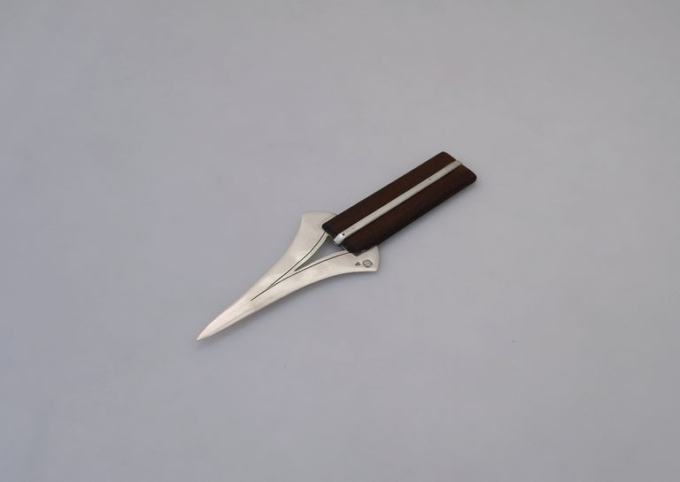 Being offered is a sterling silver letter opener by William Spratling of Taxco, Mexico, a dagger shaped blade with incised lines to emphasize the pierced triangle, a silver bar running down the rosewood handle. Dimensions: 7 3/4 inches long, 2 1/4