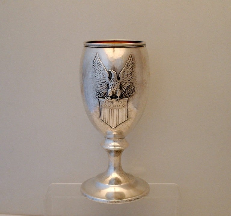 Being offered is a large circa 1916 sterling silver cup by Clemens Friedell of Pasadena, CA, handwrought, one side chased with a superb full winged eagle perched on a flag with thirteen (13) stars, the other side engraved with the dedication