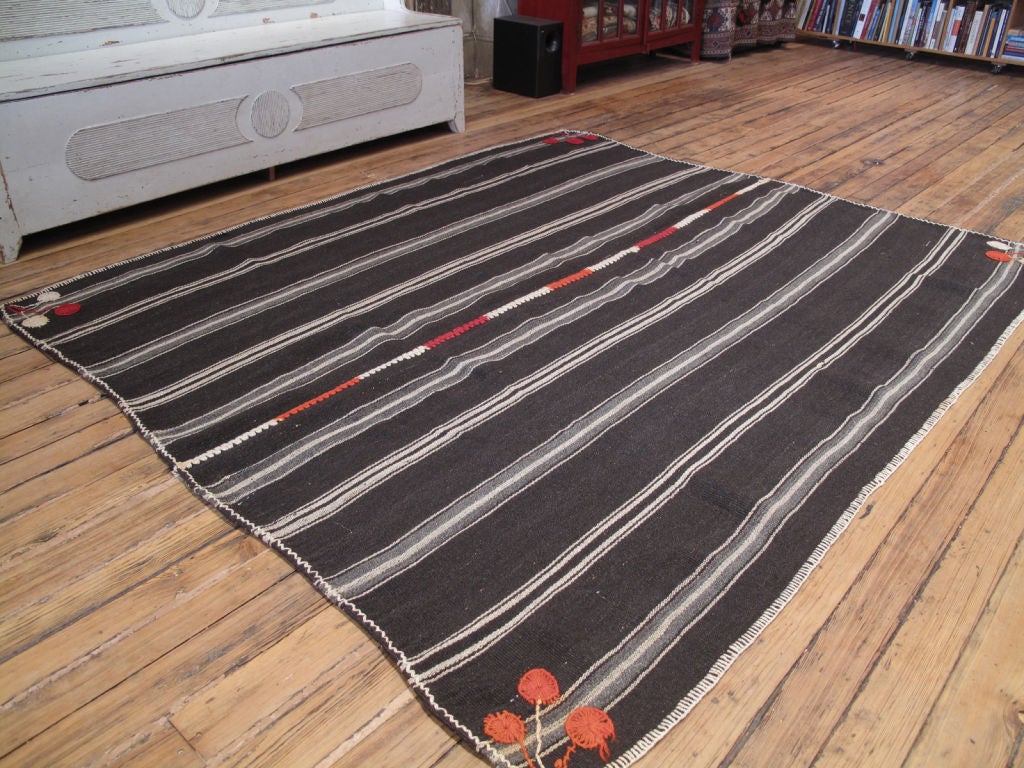 A simple tribal floor cover, made of goat hair and decorated with colorful brocading and stitching.