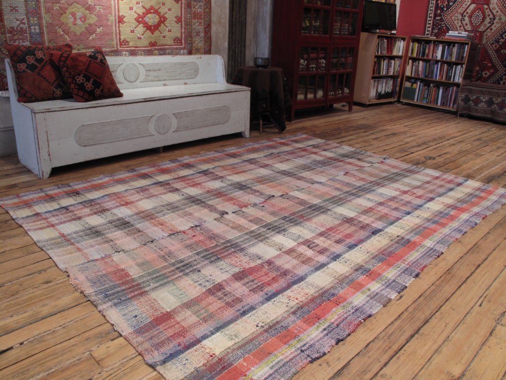 A simple, old tribal floor cover, made for everyday use, with a soft, pastel color palette. The weaving technique and use of mixed materials creates a very chic plaid pattern.