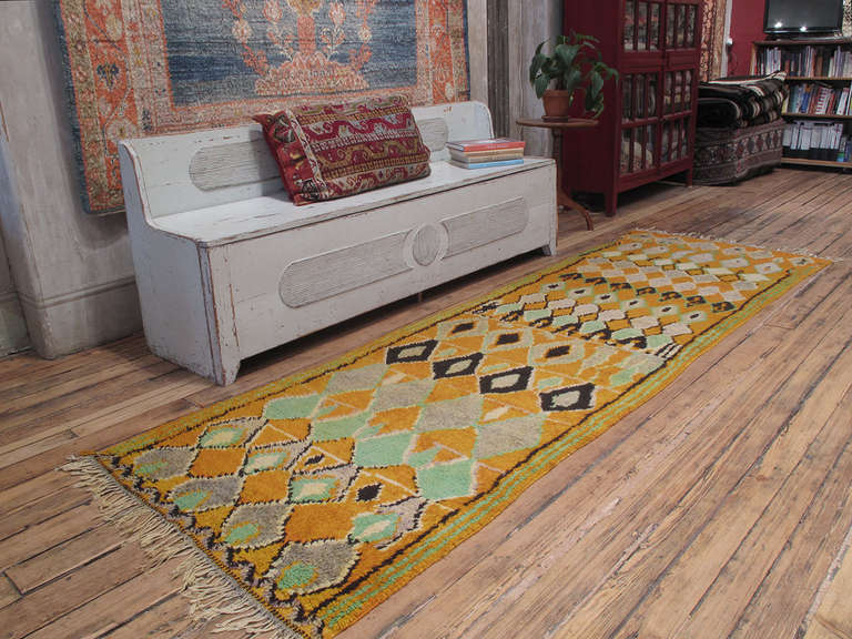 An old Moroccan Berber rug from the High Atlas Mountains in rare runner format. The yellow color is characteristic of this region and the design features a whimsical variation of diamond grid.