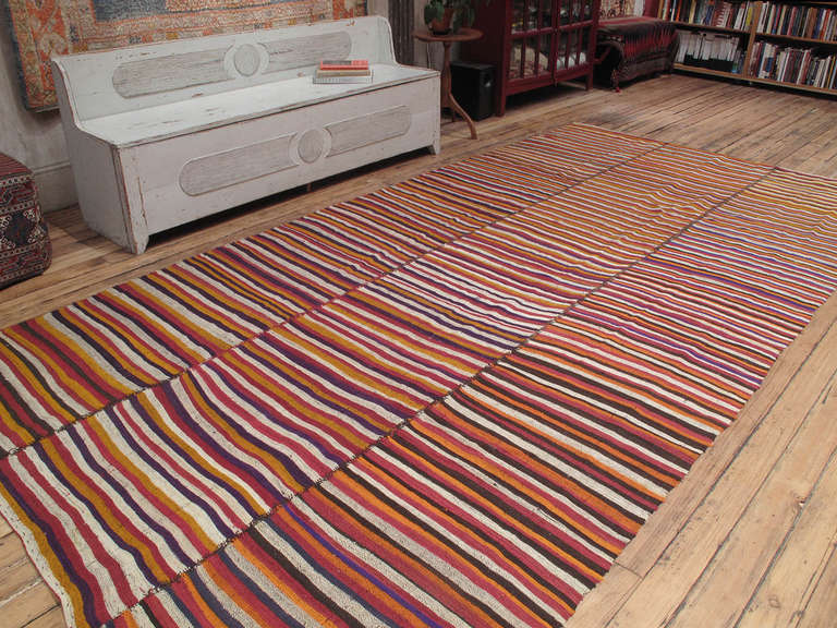 A large tribal flat-weave woven in three narrow panels. An unusually colorful example of this type with vibrant reds, oranges and even a bit of purple.