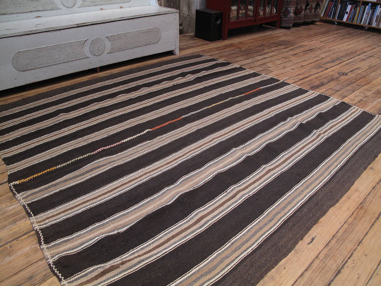 A simple tribal floor cover, woven with alternating bands of natural dark brown goat hair and thin stripes in soft colors. The piece consists of two panels joined with a heavy decorative stitch. The nearly square size format is rare in tribal