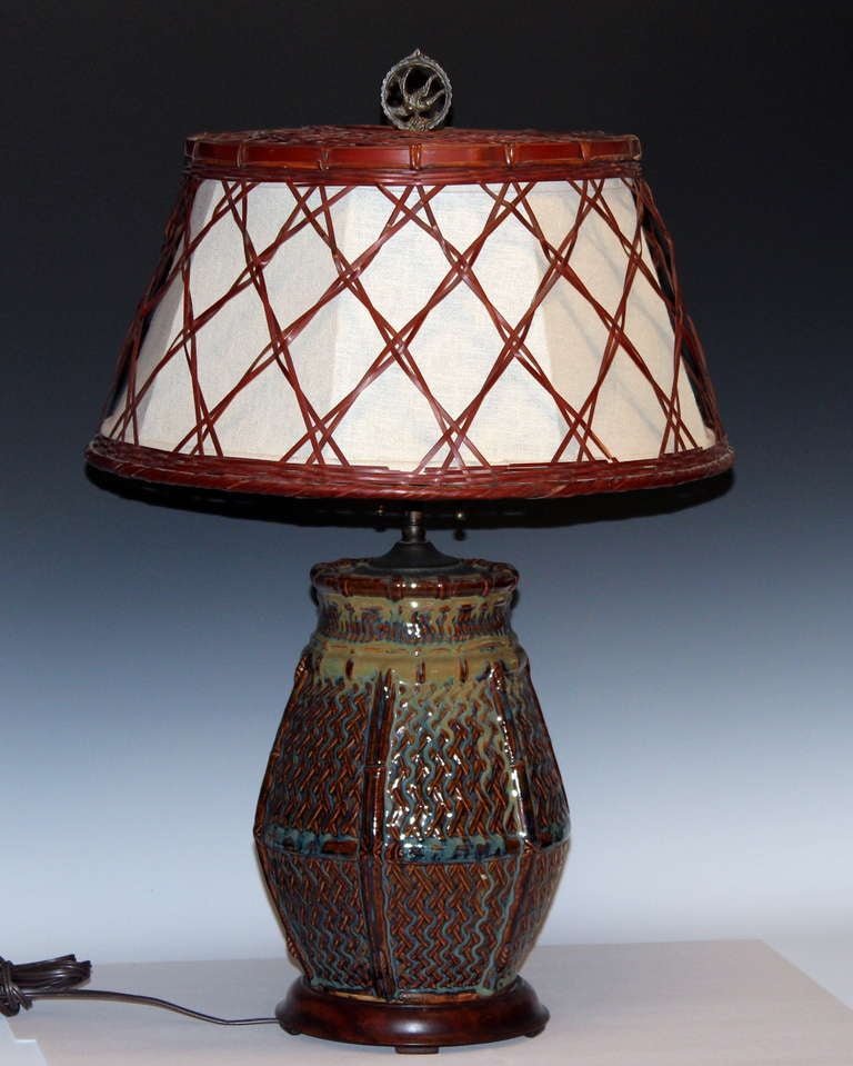 Japanese art pottery lamp in the form of a woven basket with multi color flambe glaze. Double socket, hardwood base, and period woven bamboo shade.