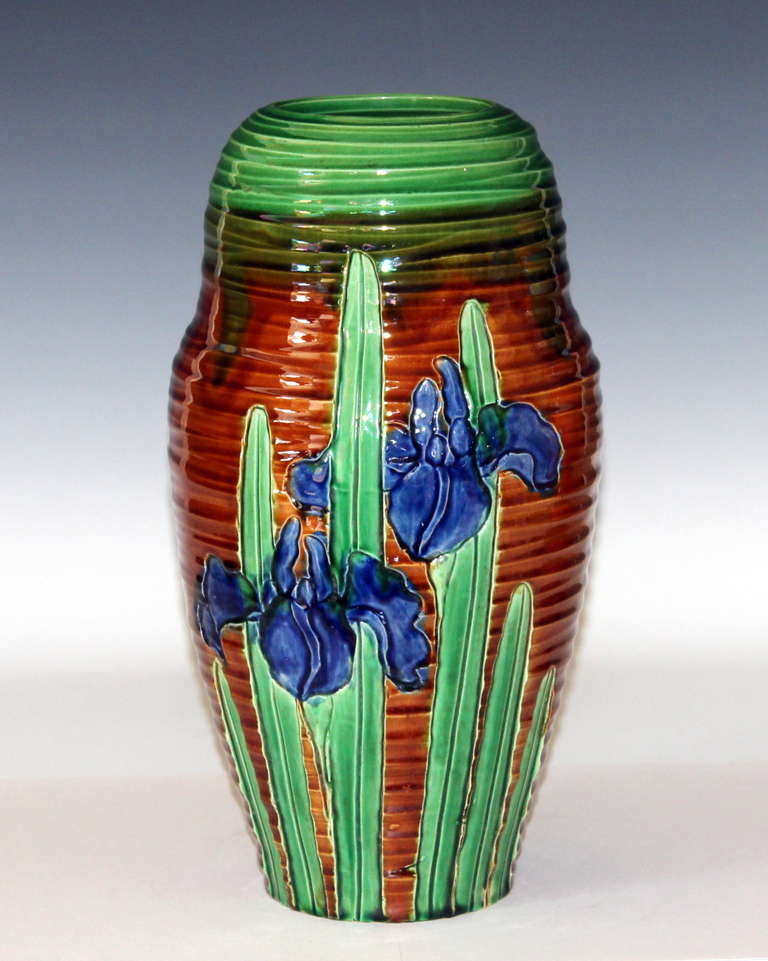 Vase en poterie Awaji avec des iris en fleurs sculptés dans des nervures accentuées. Les iris bleus et verts s'illuminent sur le sol brun chaud. Mesures : 12 1/2