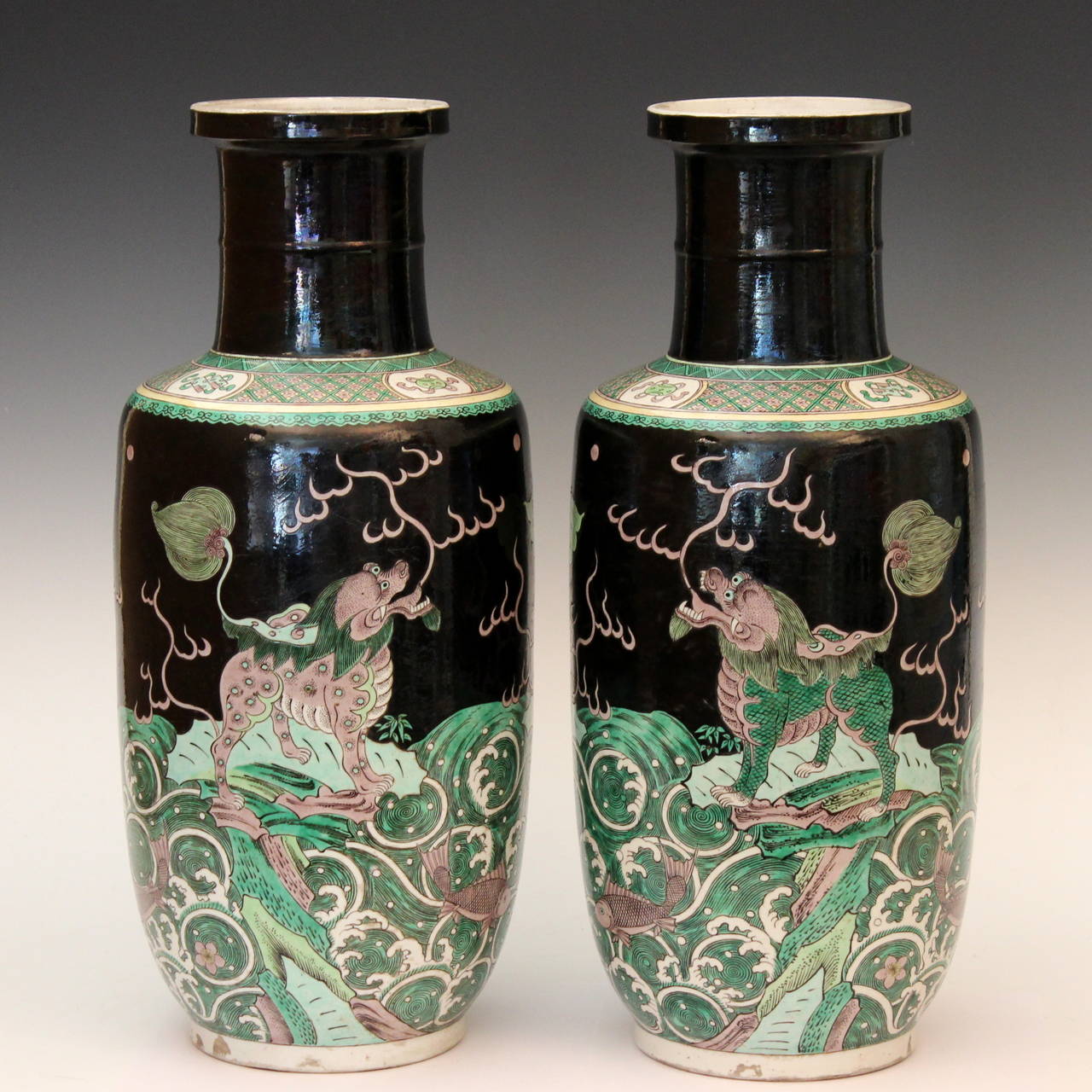 Good quality large matched pair of antique Chinese rouleau vases in Kangxi style famille noire design, circa early 20th century. Very well painted, each with three ferocious looking qilins standing on rocks above the waves, one eating a fish. The