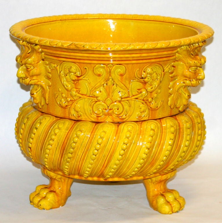 Large and dramatic jardiniere by Burmantofts Faience in Leeds, England. Elaborate form standing on hairy paw feet and guarded by blowing North Wind masks with rich, warm yellow two-toned glaze and amber glaze pooling.