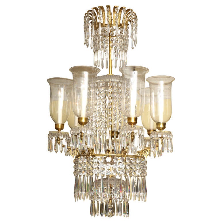 A fine Regency ormolu and cut-glass seven light chandelier, having a crown of ormolu feathers with pendant prisms and drops and a further series of four waterfalls of prisms and drops, the ormolu arms supporting shaped blown hurricane shades.