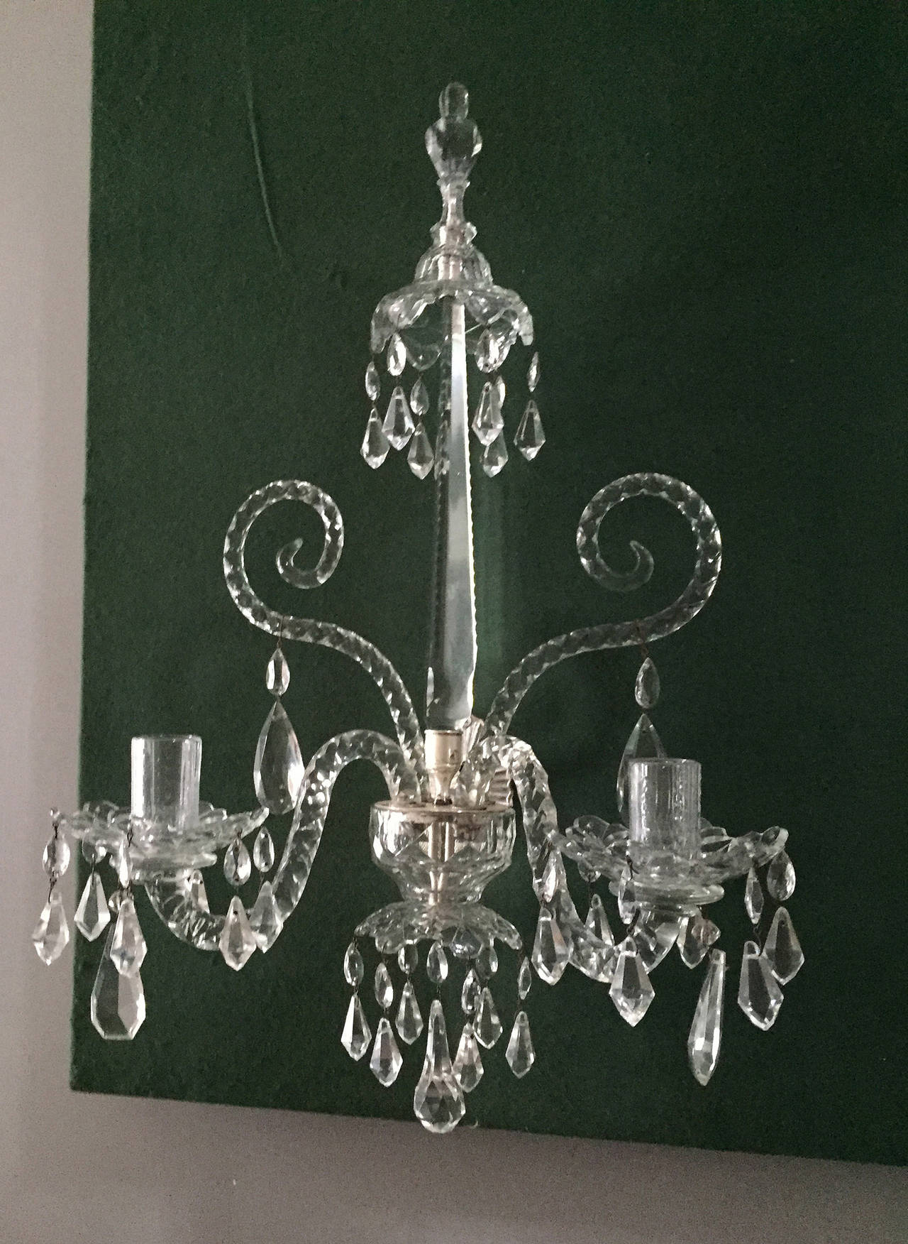 Very fine pair of antique Georgian cut-glass wall lights, having a hemispherical glass receiver cut in diamonds above a Vandyke canopy with pendant faceted drops from the tips, supported on a silvered cast brass oval sunburst ribbed wall support,