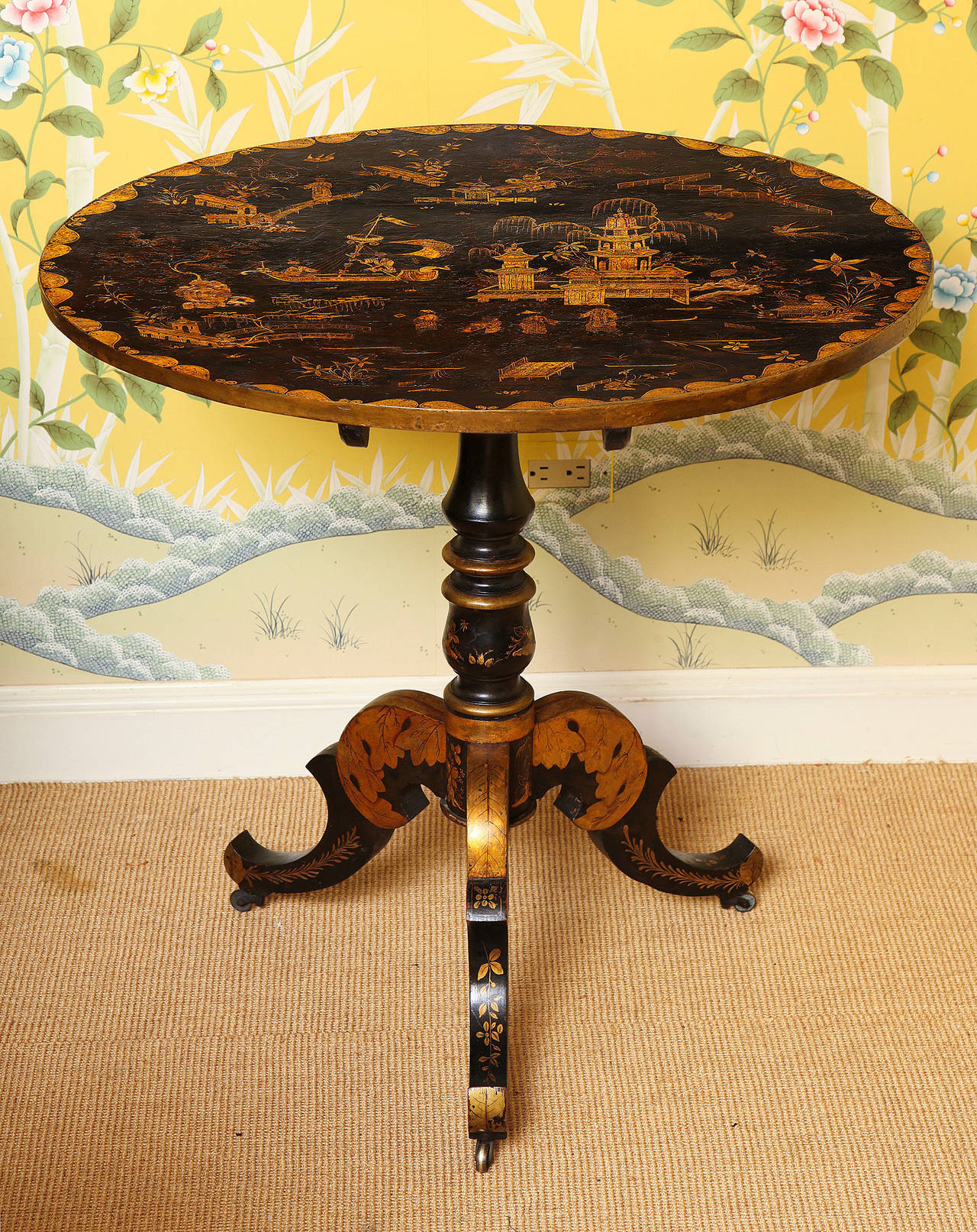 Fine Japanned chinoiserie circular tripod tilt-top table, decorated in gold, polychrome and black with scenes of a boat with figures and figures in landscapes and pavilions, etc. within a gilt scalloped perimeter, on a turned baluster standard with