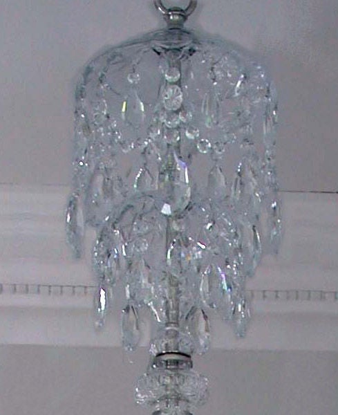 A Georgian style two tier nine light, twelve arm cut crystal chandelier with a lobed canopy above a ball stem with faceted serpentine arms alternating with spires above a lower canopy all with swags of crystal buttons and pendant drops. 

N.B. this