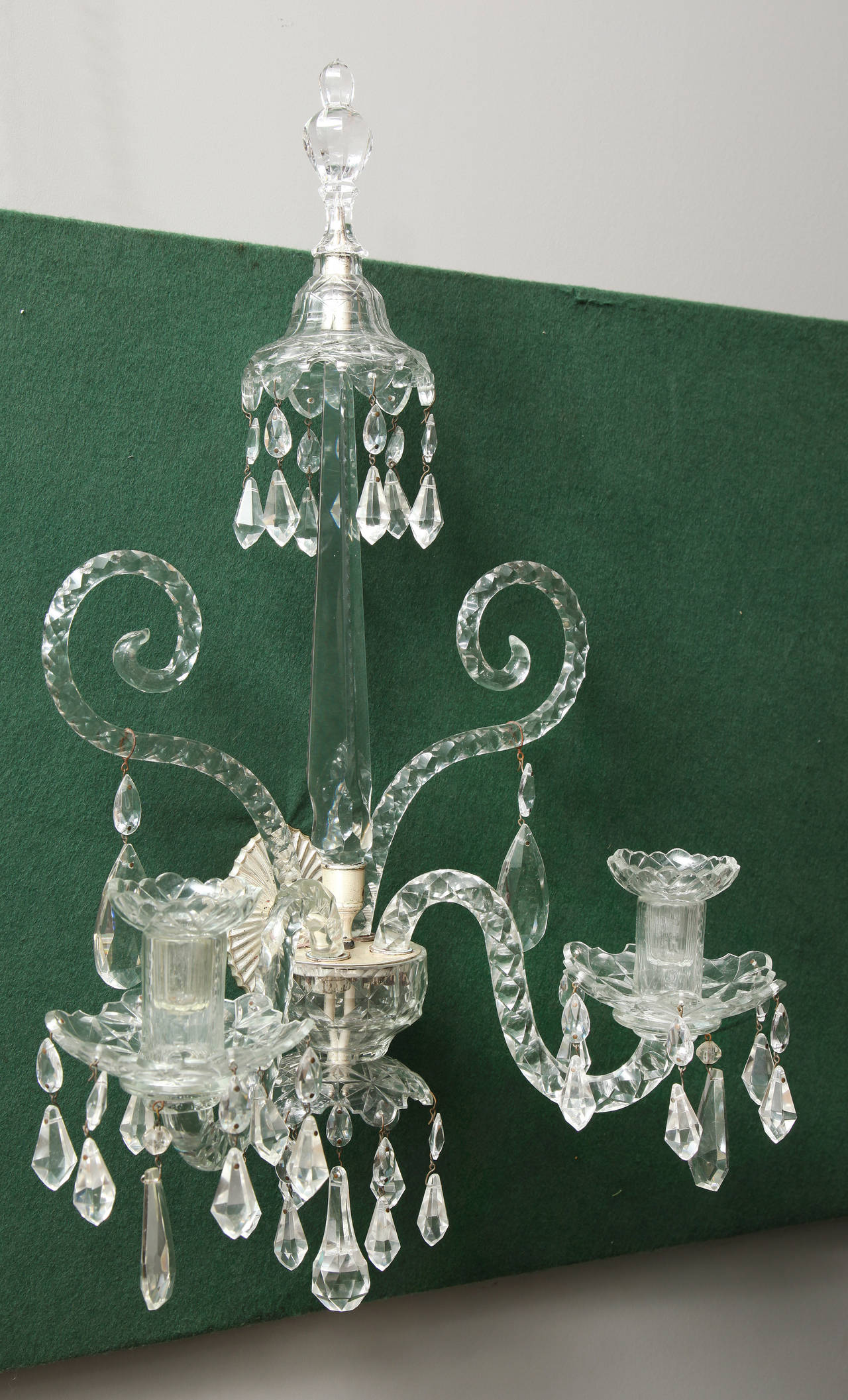Very fine pair of Georgian cut crystal wall lights, having a shaped and faceted round finial above a central spire with fine notches on the edges and centering two up-scrolled faceted glass arms with pendant drops and two S-shaped candle arms with
