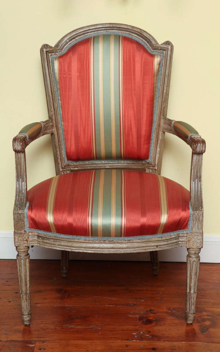 Set of four Louis XVI gray painted Fauteuils en Cabriolet, each with a shield-shaped backrest with padded armrests and scroll carved arms, having a bow front fluted apron, raised on circular stop-fluted legs headed by paterae and terminating in