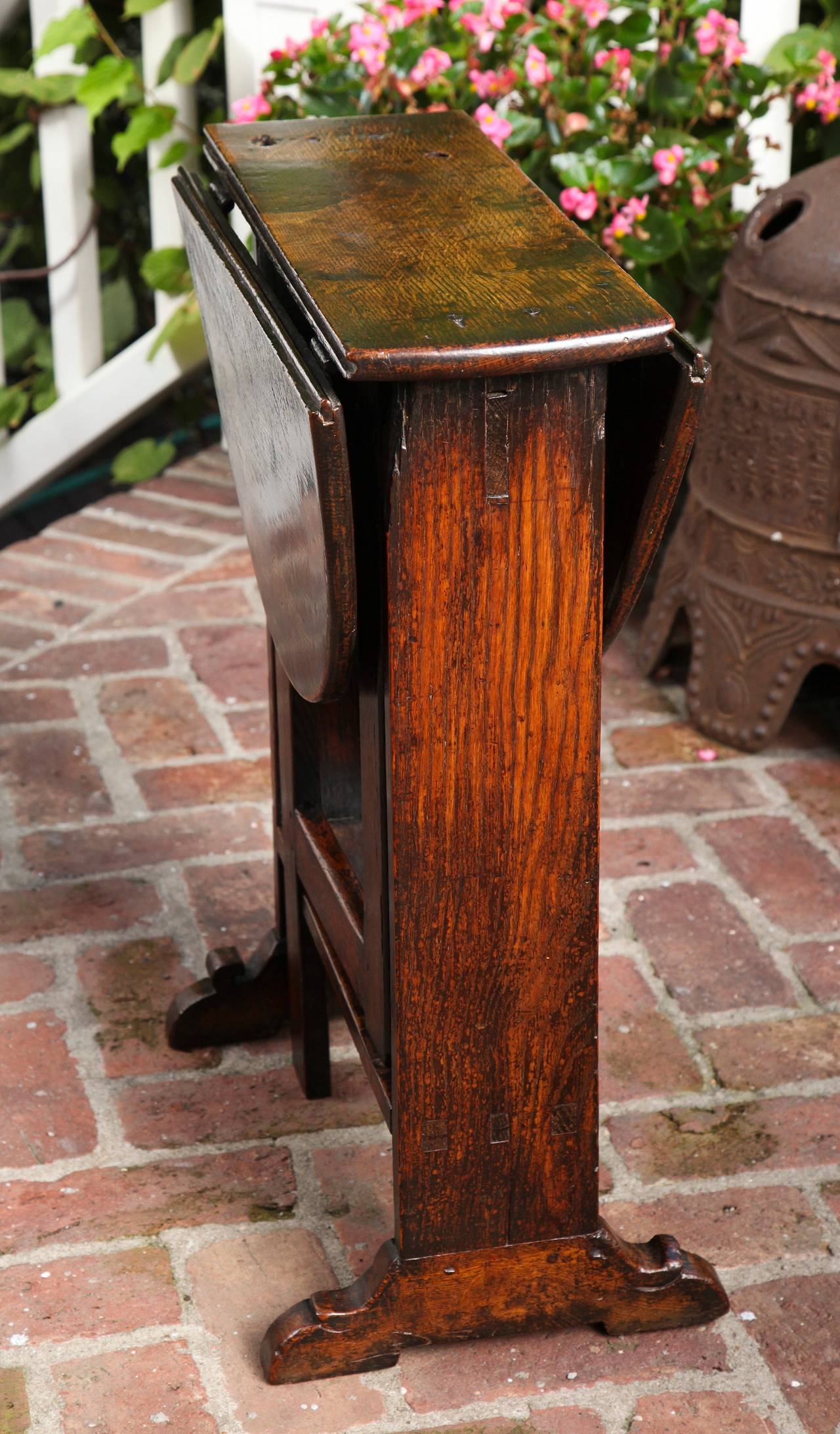 Rare diminutive Charles II solid oak gate-leg table, the beautifully patinated oval top with tongue in groove oval leaves above single plank trestle ends with sledge scrolled feet and two rectangular gate leg supports above a single plank tenoned