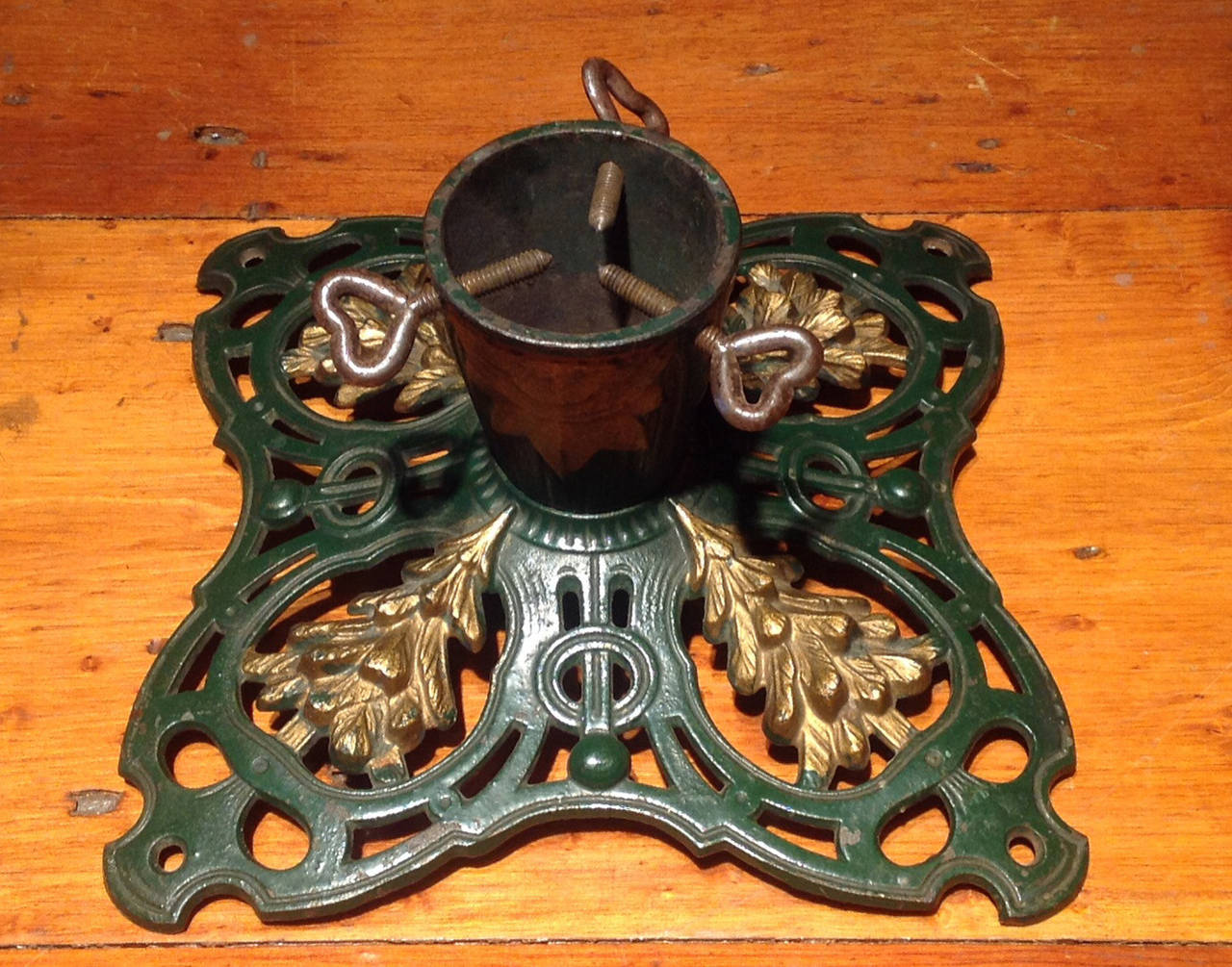 Antique Table Top Art Nouveau Cast Iron Christmas Tree Stand in Green & Gold, having three heart shaped screws above a stylized star shaft and a pierced and scroll shaped base decorated in green with four gold Christmas trees in relief.  German