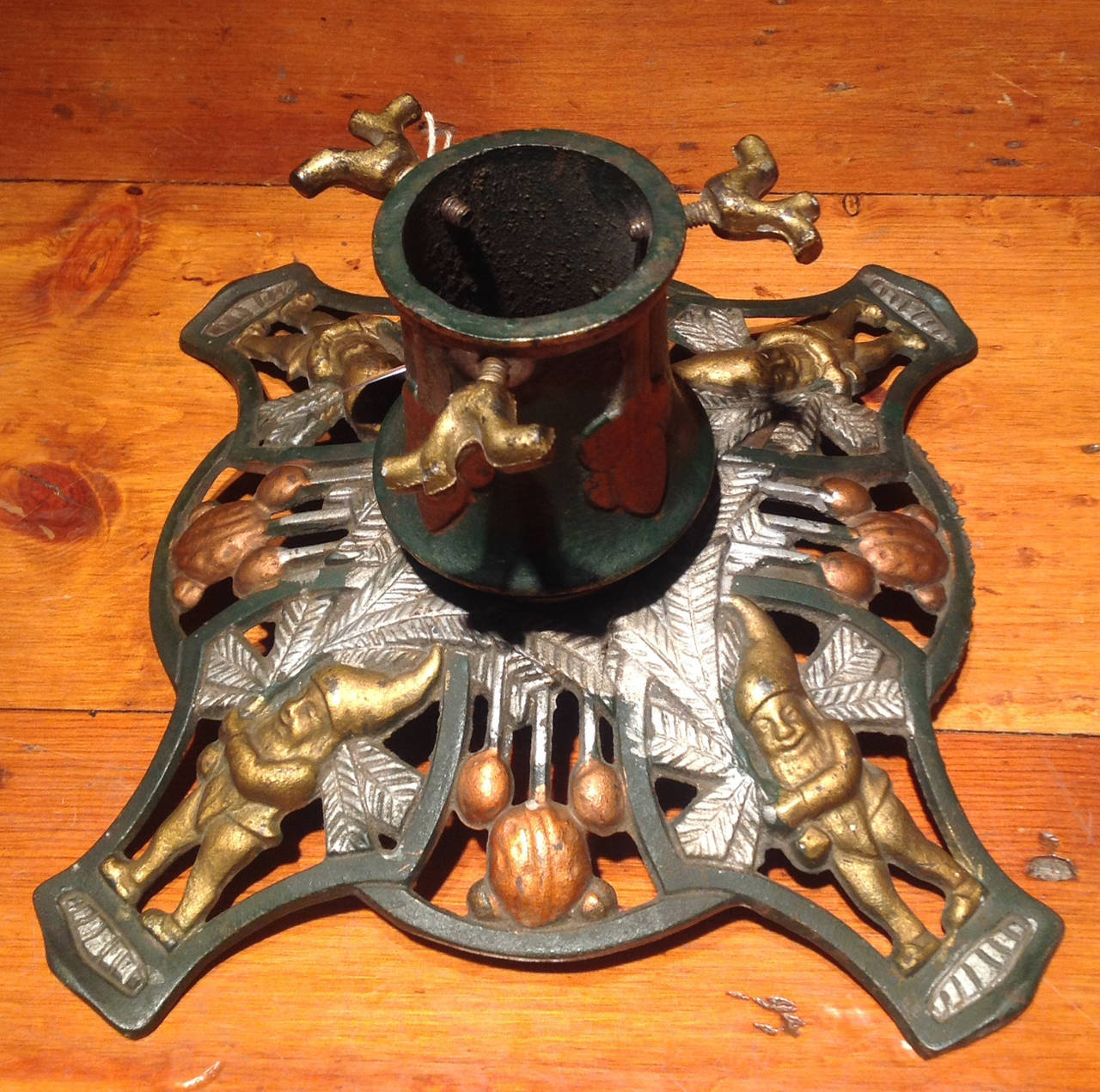 Art Nouveau Table Christmas Tree Stand having three tree branch shaped screws above a green and gilt circular shaft, having a shaped square pierced base with four gilt gnome figures holding silver pine boughs framed by register with pendant walnut,