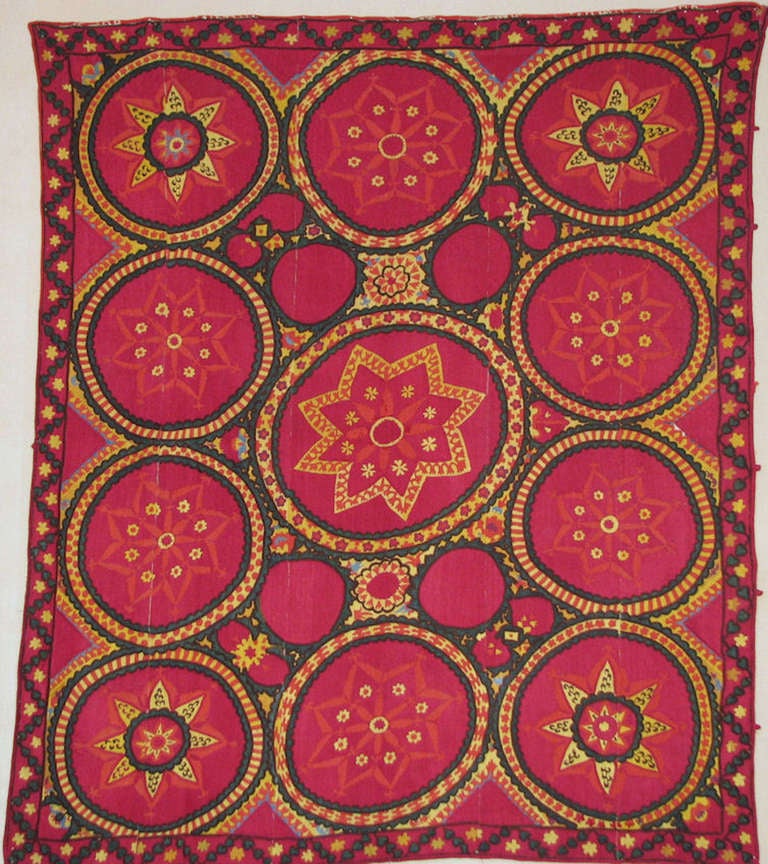 Early 20th century, Tashkent, Uzbekistan, Suzani. Embroidered in brightly colored silks of raspberry, yellow, green and black. The entire ground is embroidered in silk on a cotton ground. Eleven circles with central star like shapes fill the entire