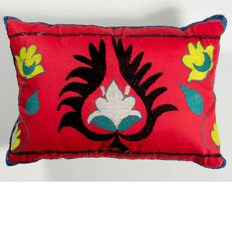 A reddish orange embroidered pillow with flower motif.