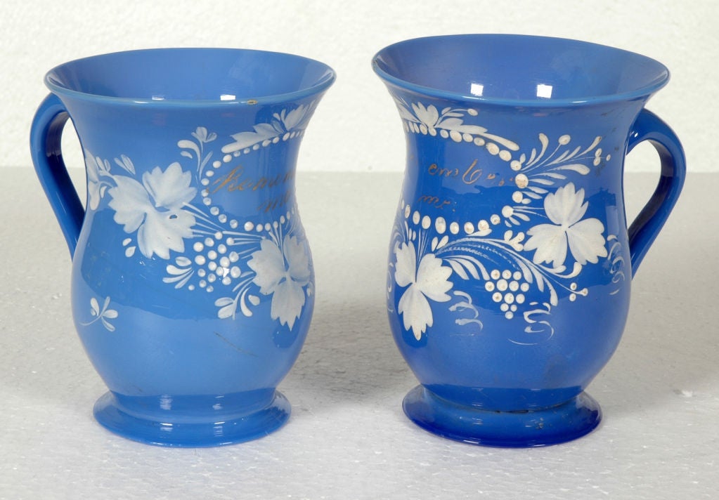 Pair of  blue blown glass mugs with applied handle and enameled white surface decoration.  souvenir of Bristol, England, circa l830.