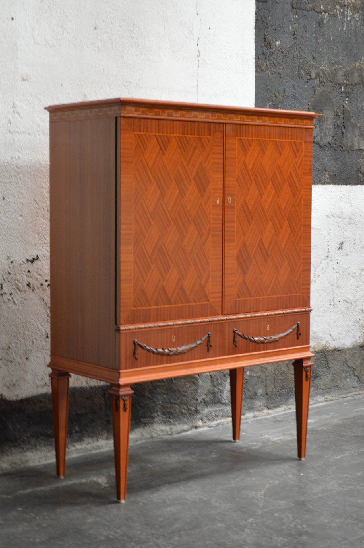 Beautiful parquetry linen or bar cabinet rendered in gorgeous ribbon mahogany. Harlequin pattern cabinet doors. Interior has four adjustable shelves and two lower large drawers. Two additional drawers with interesting carved Gustavian Style detail.