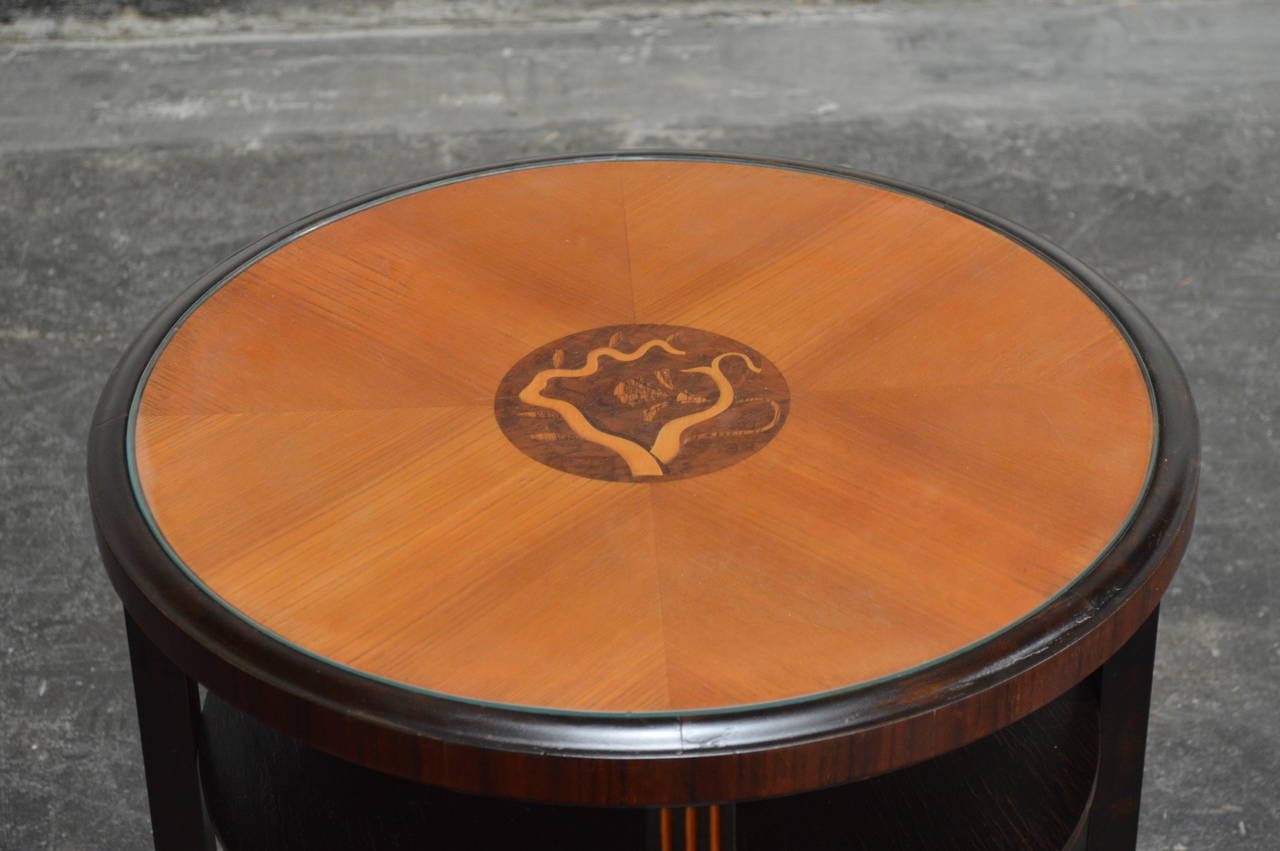 Swedish deco end or side table in golden elm and flame birch. The tabletop is paneled and inlaid with intarsia of ebonized birch, mahogany, elm and jacaranda wood protected by a piece of glass. It is the perfect size beside a club chair, at the end