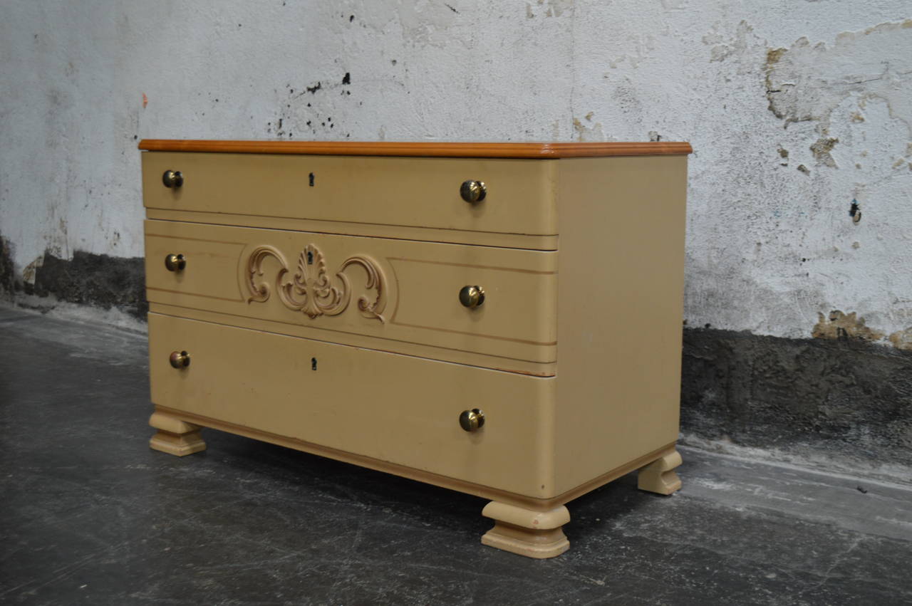 Handsome Art Deco chest of drawers. Original painted finish and golden elm top. Detailed with brass pulls, decorative centerpiece and uniquely shaped legs.