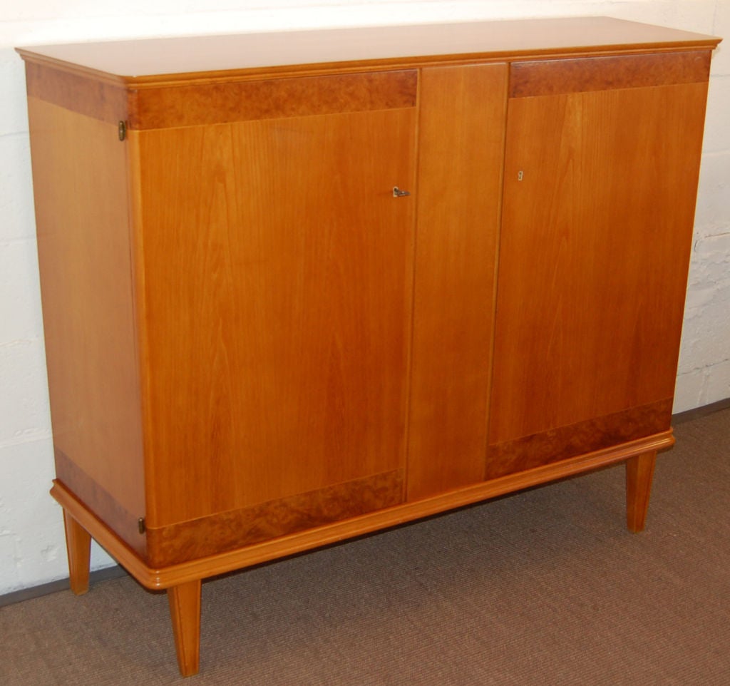 Uniquely shaped deep golden elm and Carpathian elm credenza that has mellowed to a rich amber color. Wider in the back and angled toward a more narrow front, this storage piece opens to reveal a pale golden birch interior with deep shelves and two