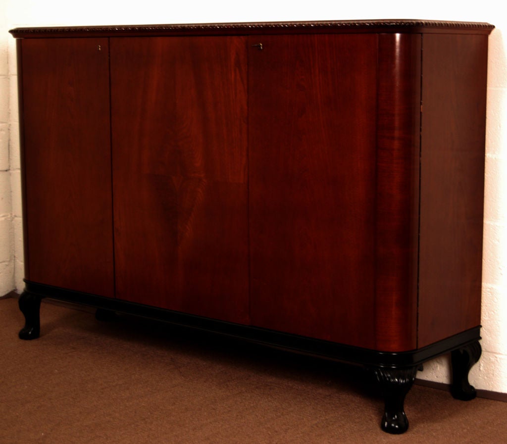 Dark elm credenza in the Art Moderne / Late Art Deco style with rounded corners and cabinet doors on a black lacquer base. Golden flame birch interior with four drawers and adjustable shelves. Key included.