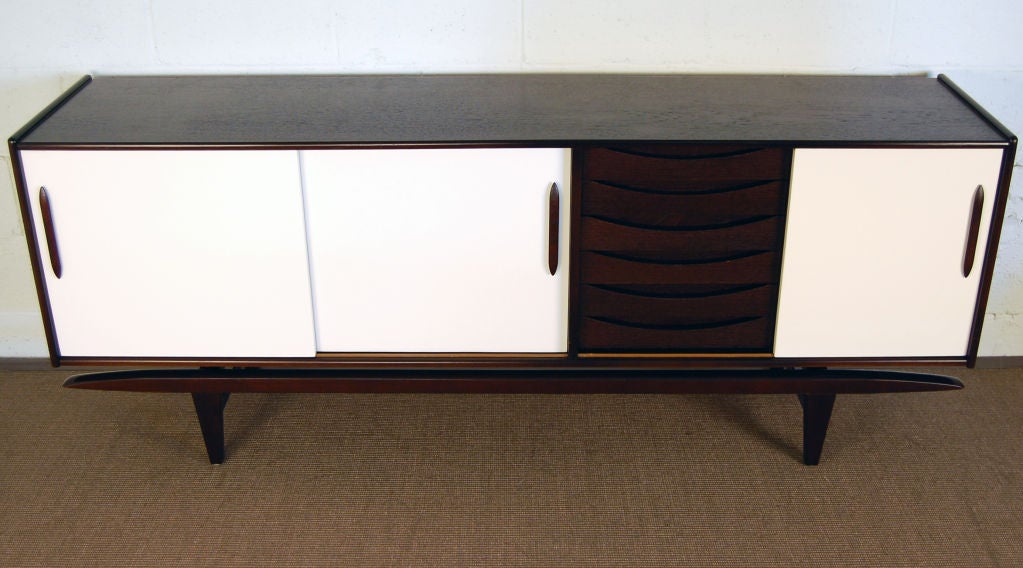 Unique credenza of natural teak with three linen white lacquered sliding doors and dark espresso brown drawers, pulls and aerodynamic base. Newly restored and in fantastic condition. This cabinet features six beautifully convex curved dovetailed