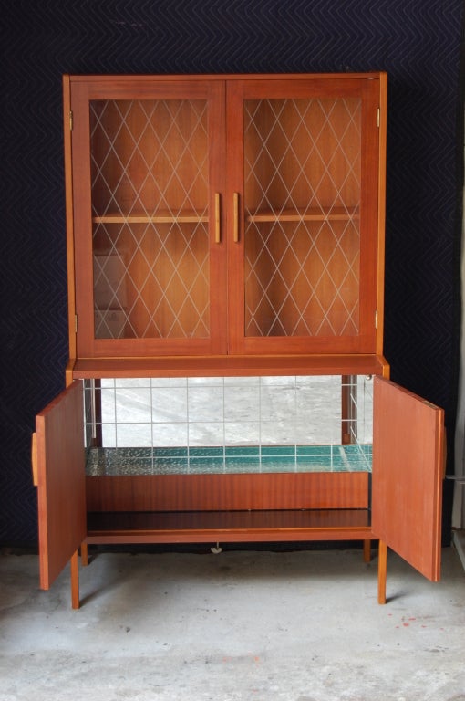 Swedish Mid-Century teak bar cabinet. Lower locking doors open to reveal a lighted glass shelf and etched mirrored glass. Upper cabinet has two etched glass doors with bar storage with a shelf for glassware storage. In excellent original condition.