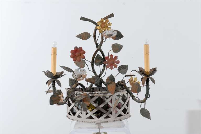 A pair of iron and tole painted sconces with flowers and arms extending from an openwork half basket.