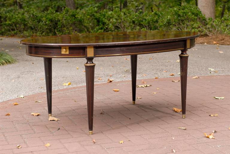 A fabulous Louis XVI style dining table attributed to Masion Jansen, circa 1940s. Beautiful flamed mahogany with a subtle cordovan tone. Tapered fluted legs with bronze accents. Apron with bronze detail and classic match strike insets. Leaves are