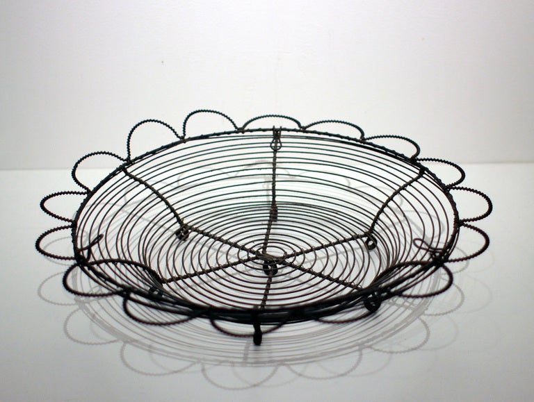 Shallow steel wire basket with a decorative scalloped rim, feet and removable hanger; late 19th century, American.