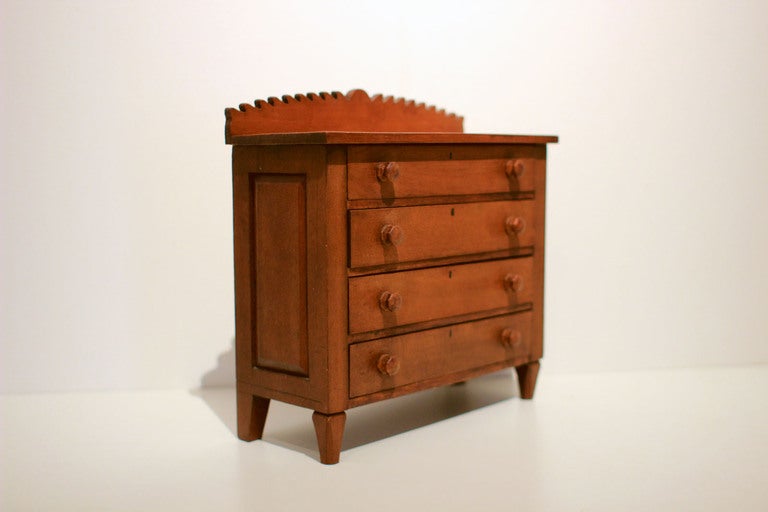 Miniature cherry chest with carved backsplash, drawer knobs and details, and painted keyholes; American, circa 1850.