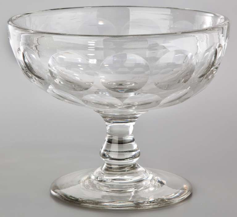 This fine and generous handblown, colorless glass compote features two rows of cut bull’s eyes around the bowl and a well-proportioned, applied base. Good, appropriate wear is visible on the bottom edge, and a very clean pontil is found, which