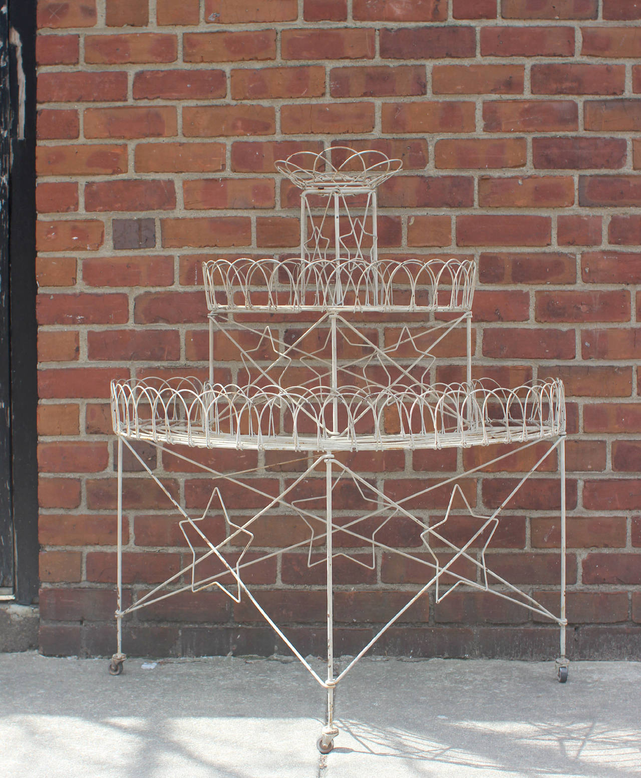 Sturdy steel wire three-tiered plant stand with large scalloped edging and, unusually, with decorative stars; original casters and paint, American, circa 1890.