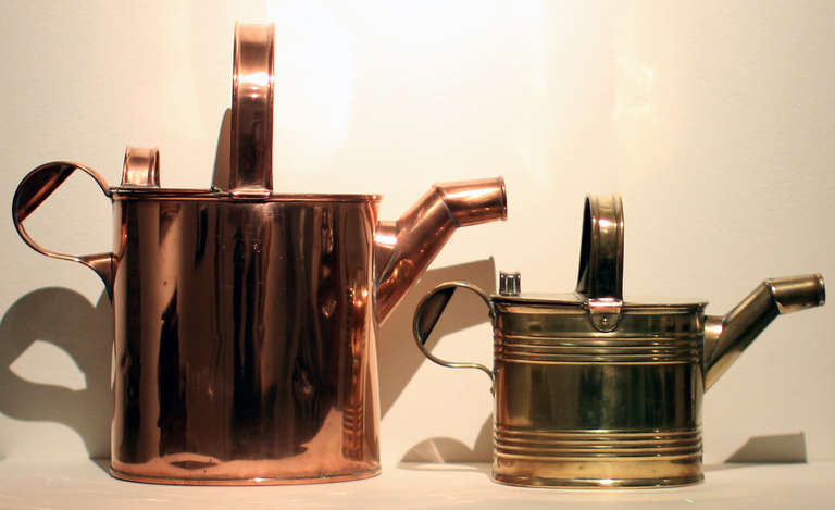 Two watering cans - a larger copper-plated tin one and a smaller brass-plated tin one with ribbed detail. Both soldered and the brass is reinforced with tacks. Same great form for each, and both are late 19th century English. The smaller brass one